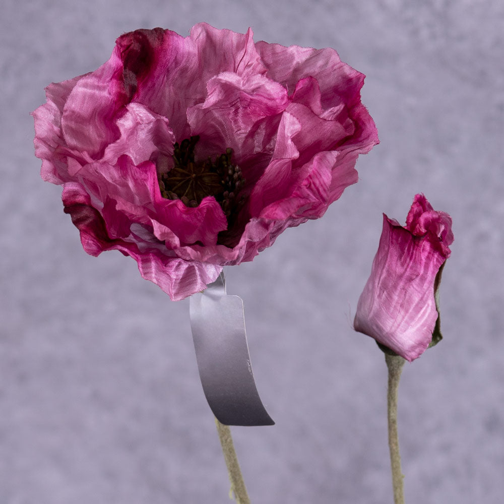 A faux poppy stem with an open flower and a budding flower on two branchlets. The flowers are a dark pink colour with purple tones