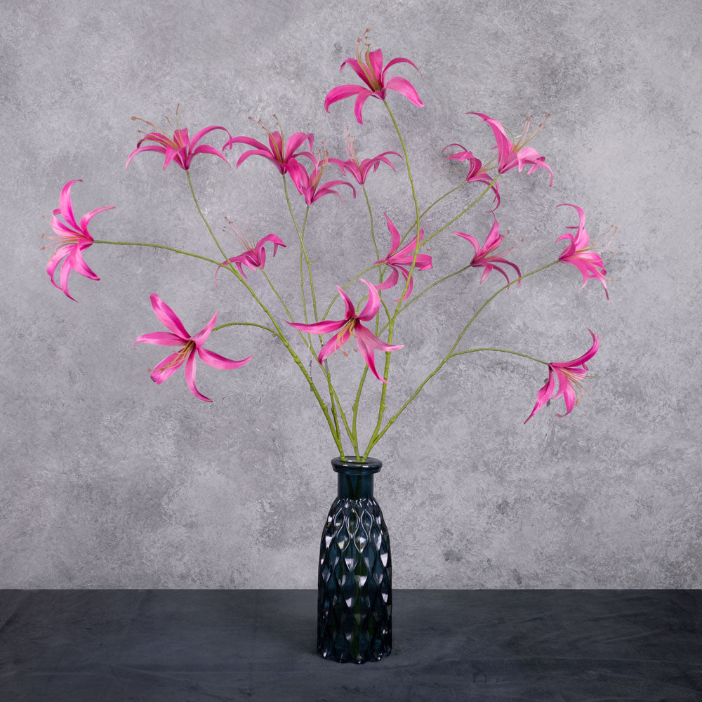 Three tall. faux lily sprays with bright pink flowers, shown in a dark blue glass vase