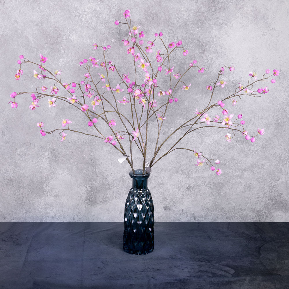 Three faux thalictrum sprays covered in strong pink flowers, shown in a blue glass vase