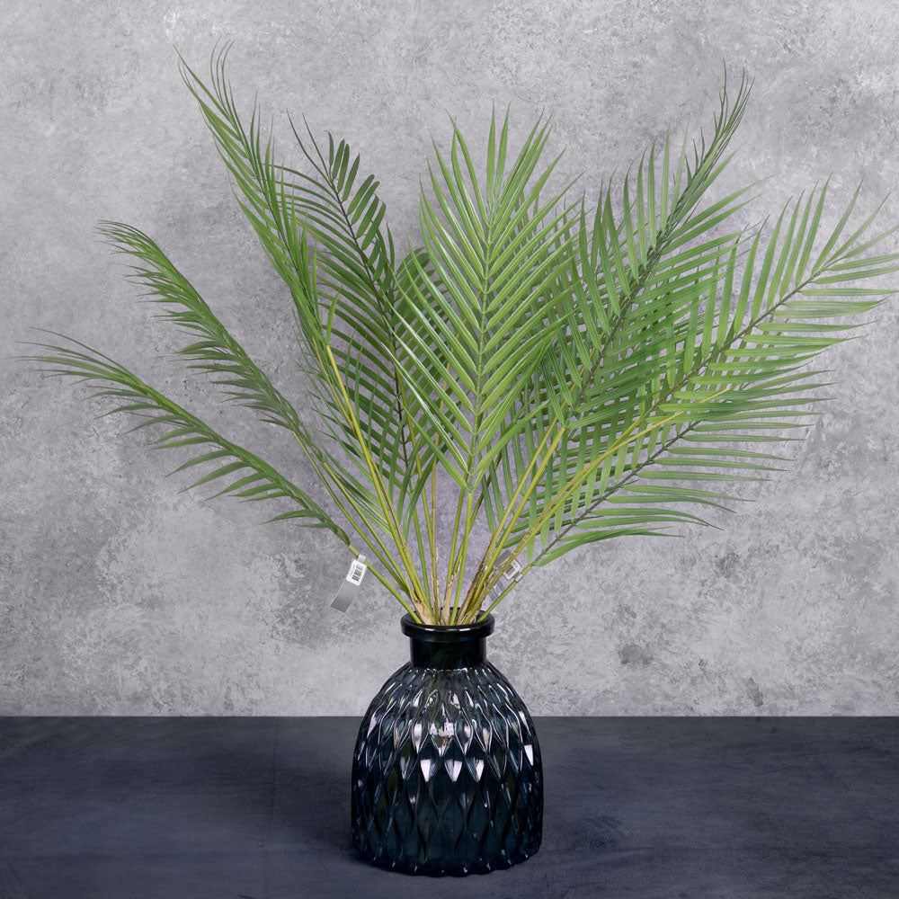 A group of three faux palm bushes in green, displayed in a blue glass vase
