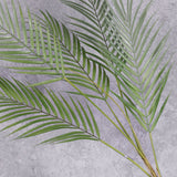 A close up of a faux, green palm bush with one main stem and three fronds