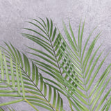 A close up of a faux, green palm bush with one main stem and three fronds