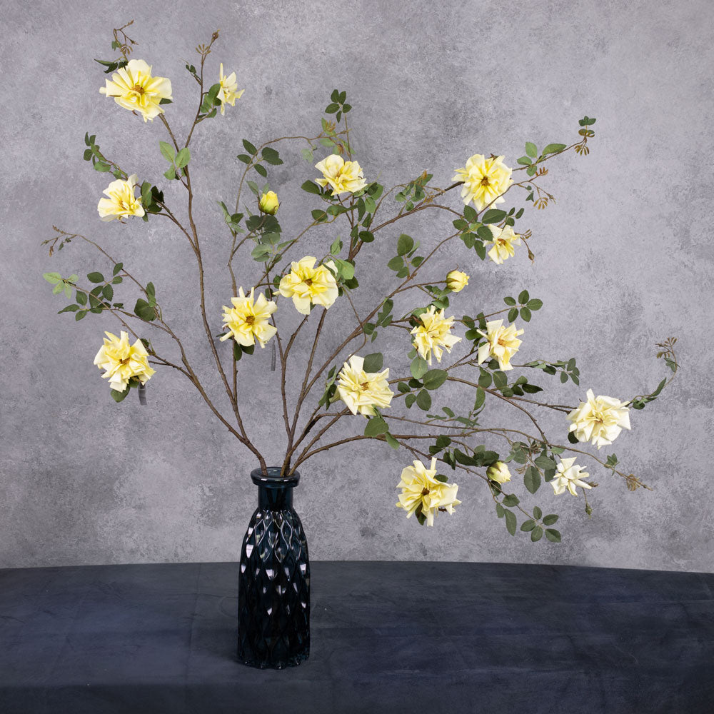 3 individual A faux yellow rose spray branches displayed in a blue, glass vase.