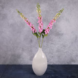 Three individual faux, pink foxglove stems in a cream, oval vase