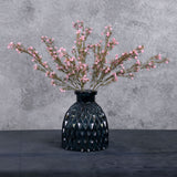 Three faux gypsophila stems, in light pink, sat in a blue glass vase