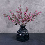 A group of three faux gypsophila sprays in deep pink, sat in a blue, glass vase