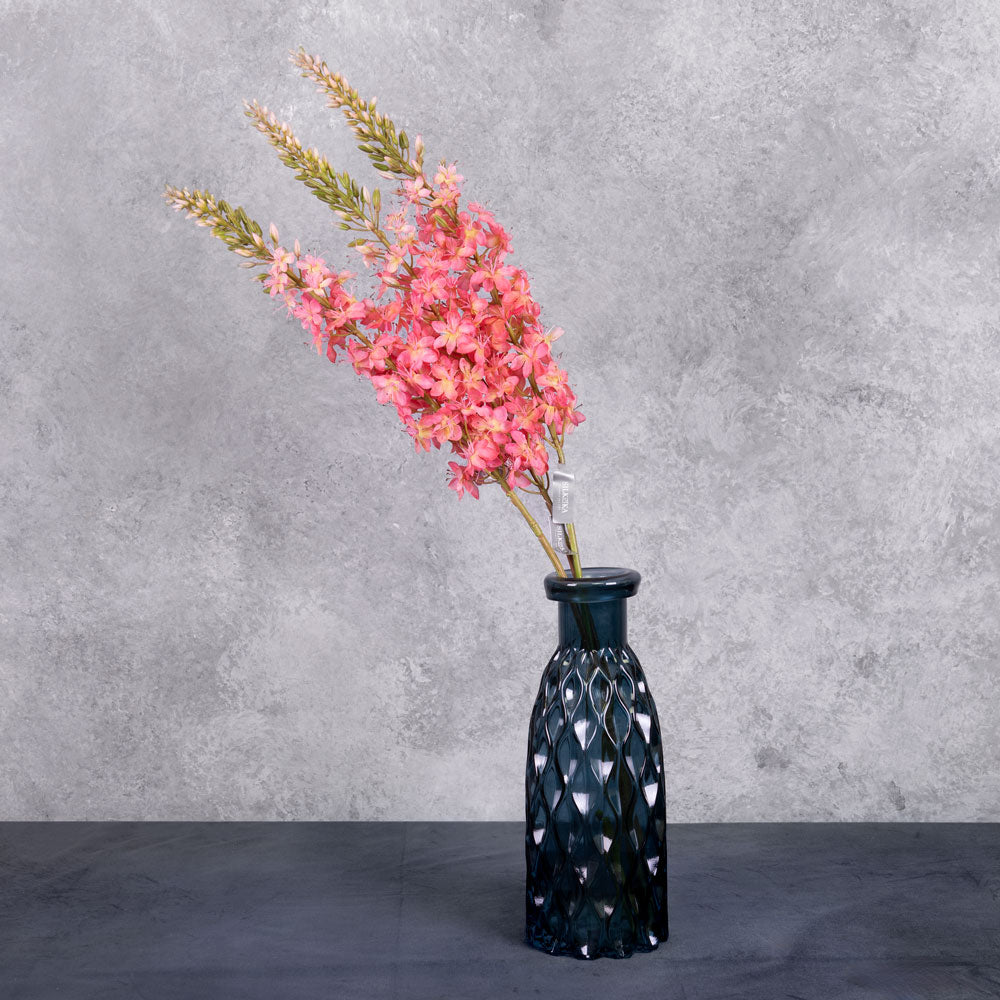 Three faux, fox tail lilies in a warm pink colour, shown in a blue glass vase