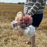 A collection of pastel coloured Silk-ka faux flowers, held against a cloudy sky and stubble field.