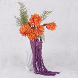 Mauve amaranthus displayed in a white vase along with faux orange flowers and green fern fronds.