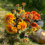 A group of different coloured, sized, and shaped faux sunflowers, displayed in a meadow against a bright, sunny sky