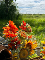 A group of different coloured, sized, and shaped faux sunflowers, displayed in a meadow against a bright, sunny sky