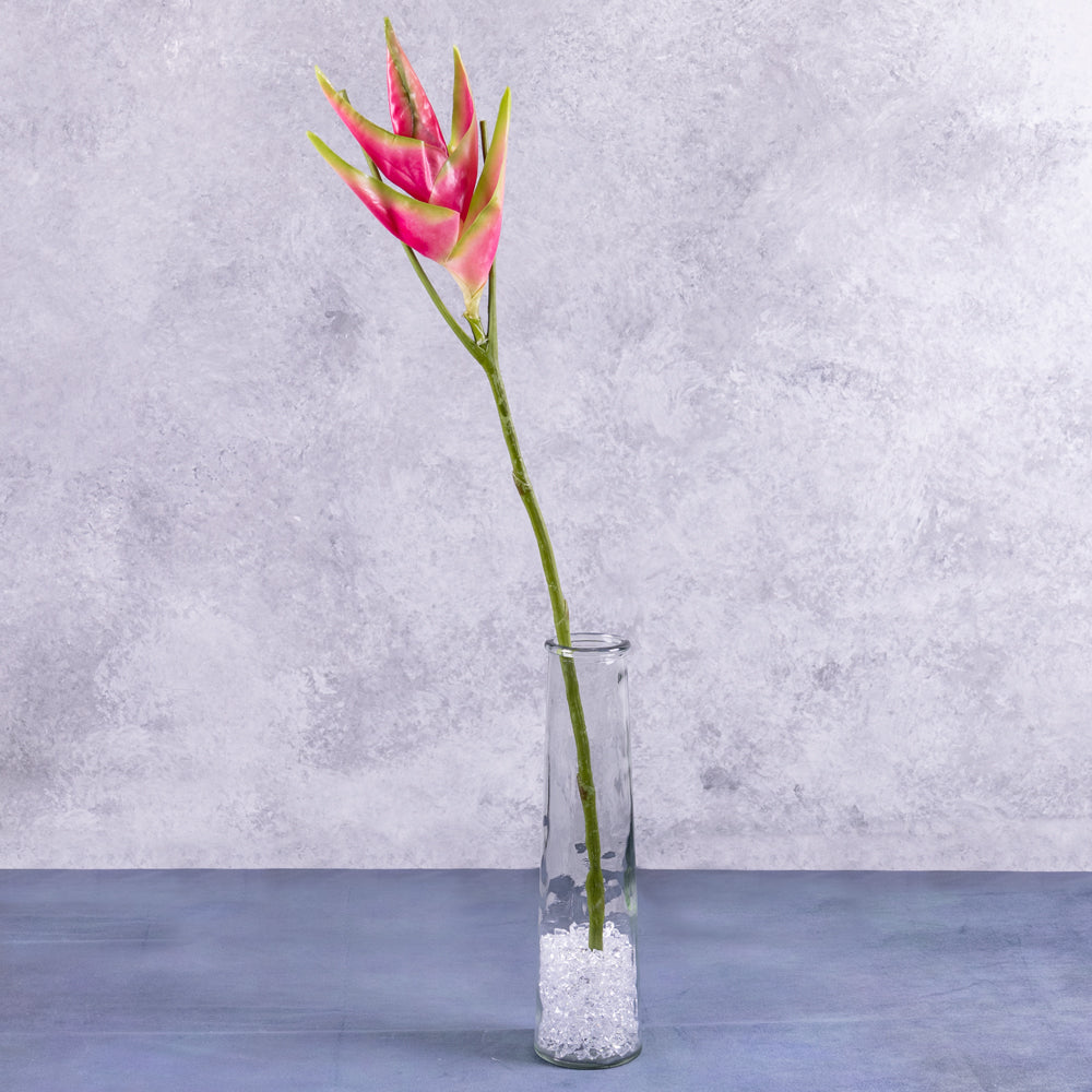 An artificial heliconium flower in bright pink, displayed in a clear glass vase