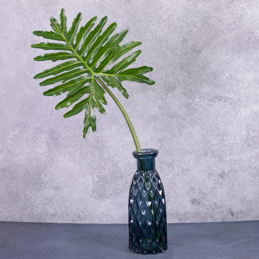 A faux Philodendron selloum leaf displayed in a blue glass vase