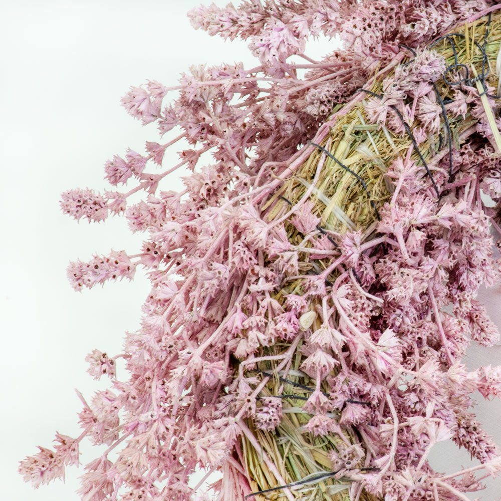 a wreath made of linen herb and painted a chalky pink colour, against a white background