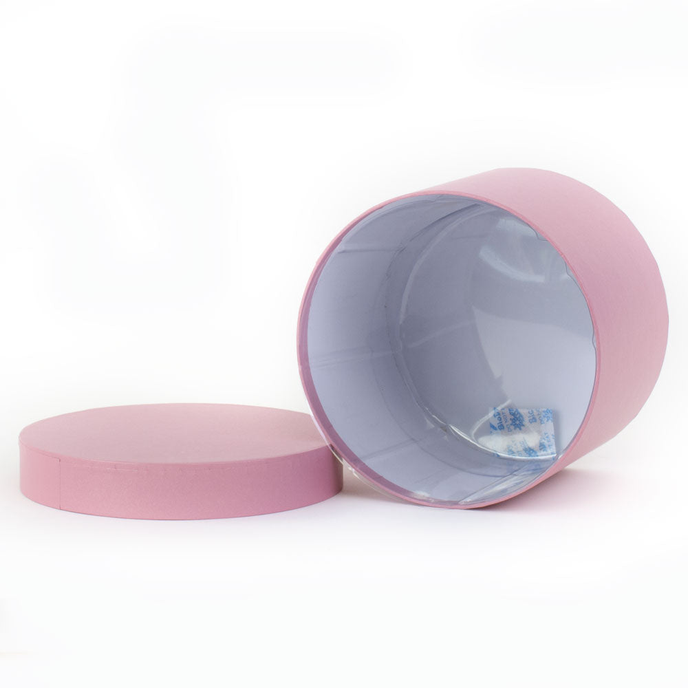 a baby pink coloured hat box laying on its side with the lid to one side