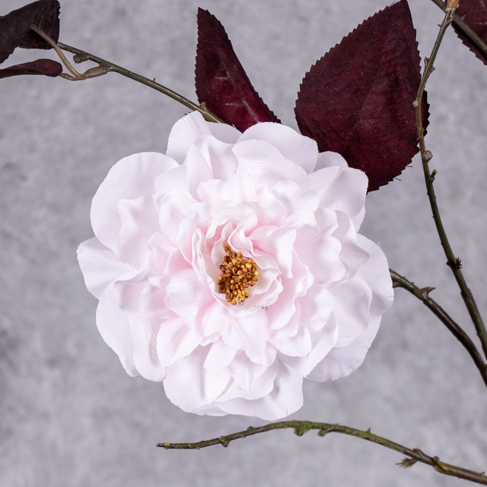 A close up of a faux camelia spray, in white with red leaves
