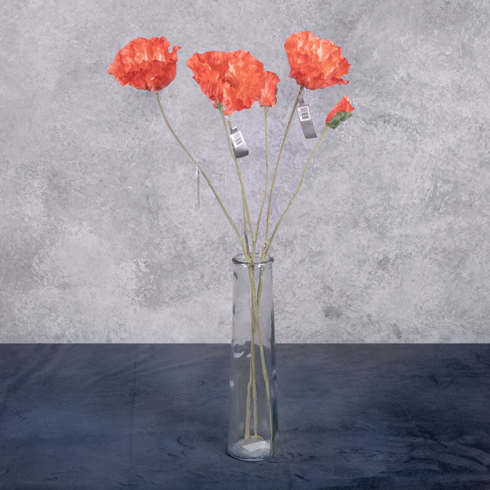 Three faux poppy stems, with a flower and bud in a delicate reddish orange colour om each stem, in a clear glass vase