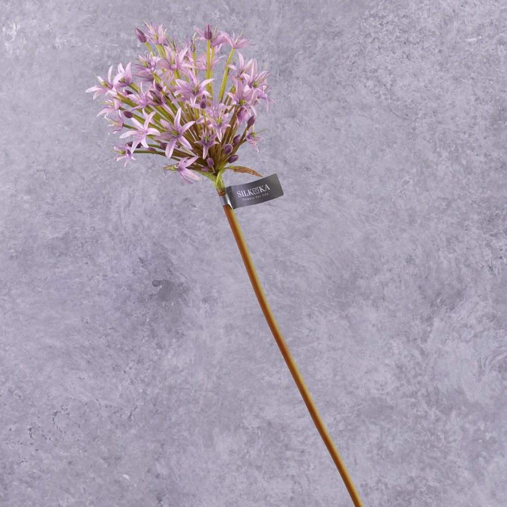A group of three faux allium stems with lilac coloured flower plumes, displayed in a blue glass vase