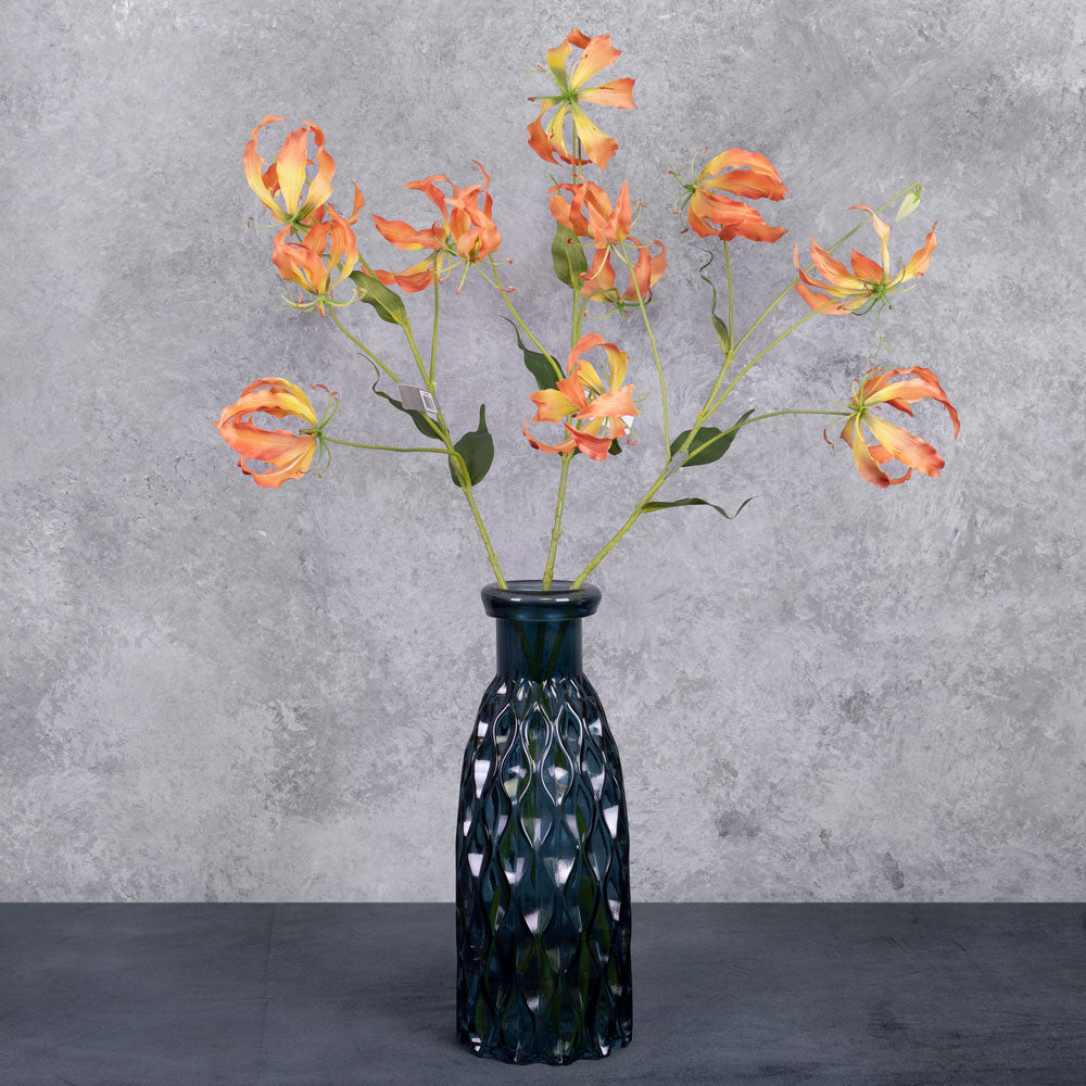 A group of three faux gloriosa sprays with orange-yellow flowers, displayed in a blue glass vase
