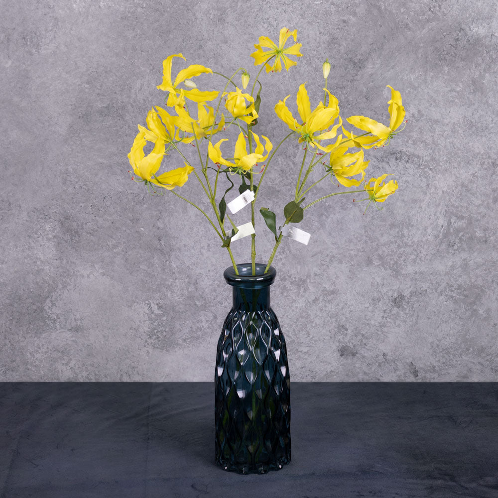 A group of three faux gloriosa sprays with yellow flowers, displayed in a blue glass vase