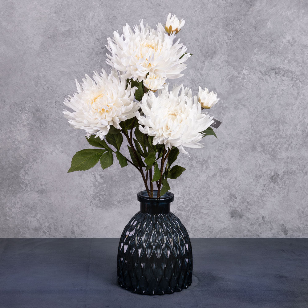 A group of three faux chrysanthemum sprays in an off-white colour, displayed in a blue glass vase
