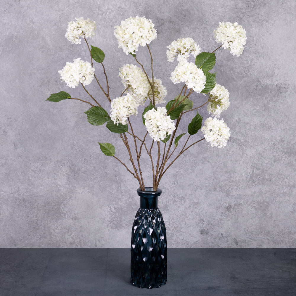 A close up of a faux, cream hydrangea flower that looks like a pom pom, showing leaf detail