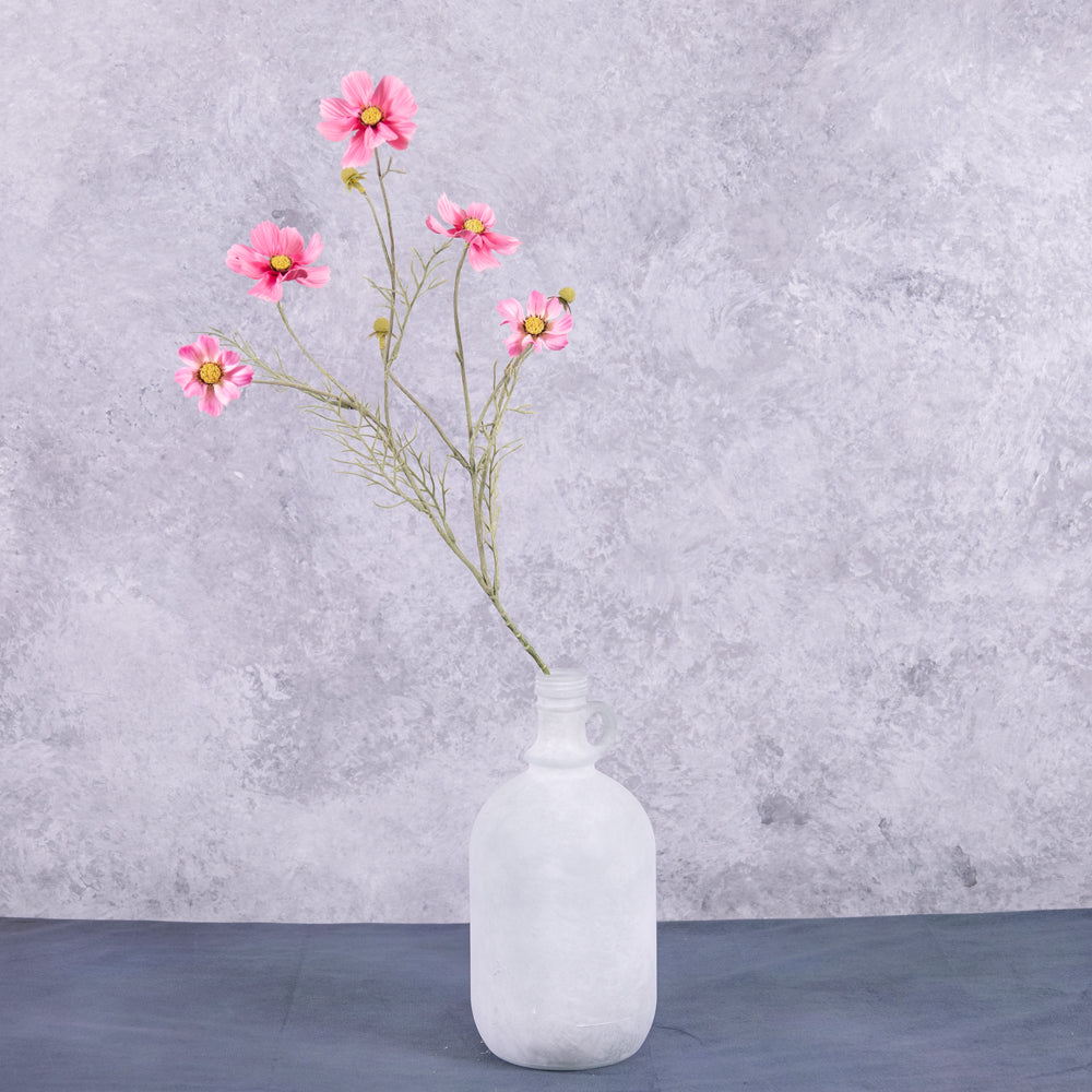 A pink cosmos flower spray displayed in a white frosted glass demi-john
