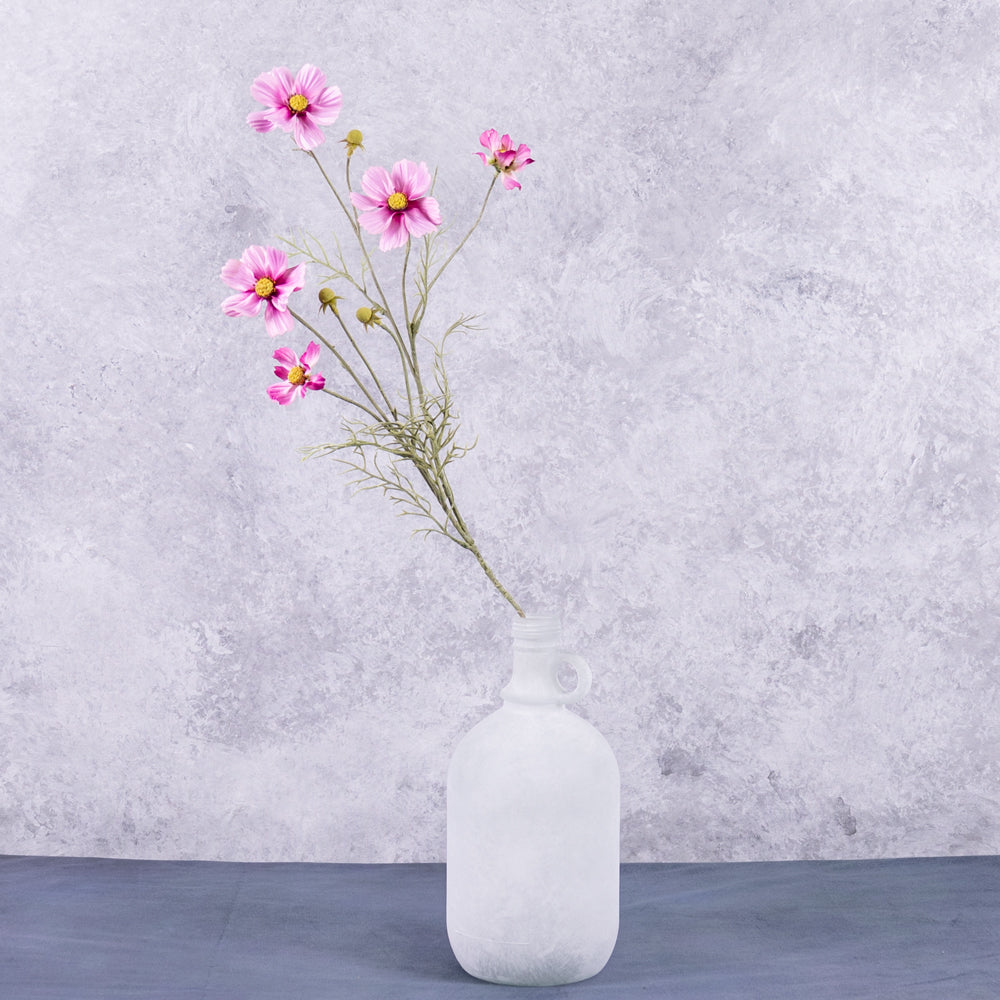 A pink cosmos flower spray displayed in a white frosted glass demi-john