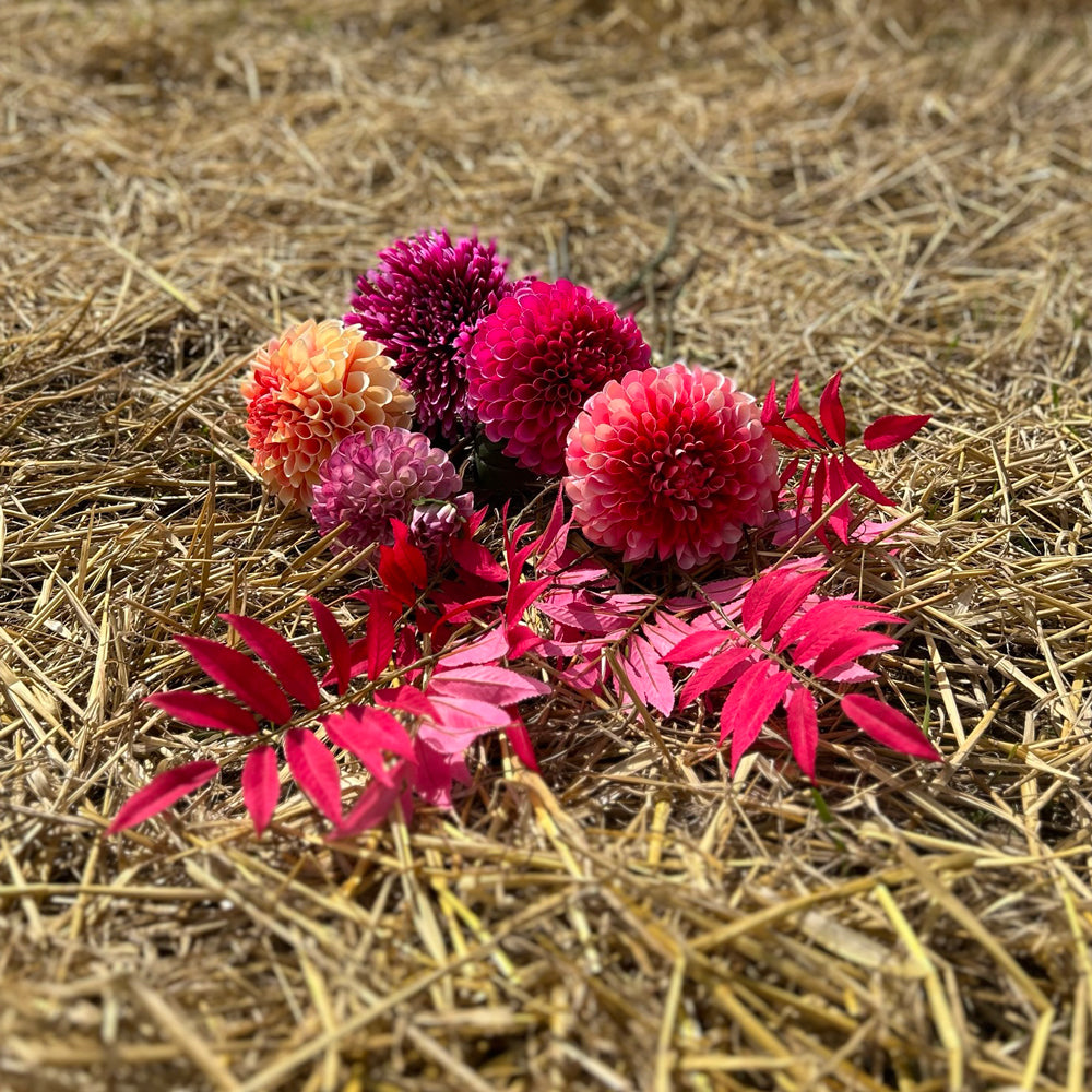 A collection of Silk-ka artificial flowers and foliage in different shades of pink laid on a stubble field.