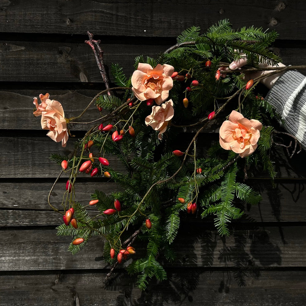 A long, artificial pine garland show in a circular shape along with a faux rose and berry spray