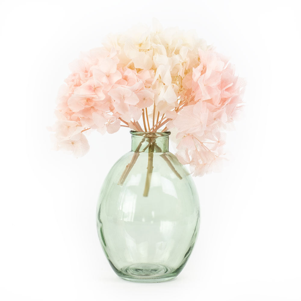 A translucent green glass vase displaying some preserved hydrangea flowers